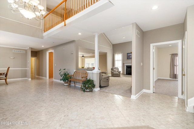 foyer featuring a high ceiling, light carpet, ornate columns, and ceiling fan with notable chandelier