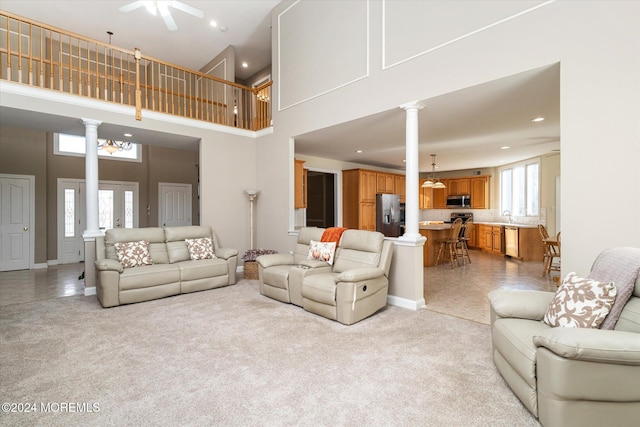 carpeted living room with ornate columns, a towering ceiling, ceiling fan, and sink