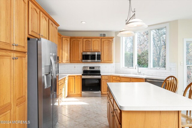 kitchen featuring stainless steel appliances, decorative light fixtures, decorative backsplash, sink, and a center island