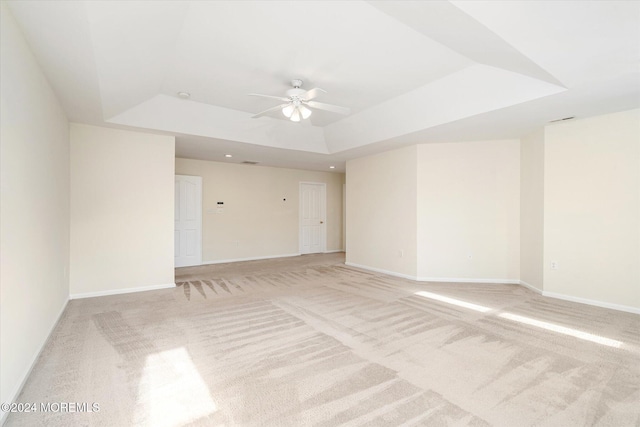 spare room featuring ceiling fan, light carpet, and a raised ceiling