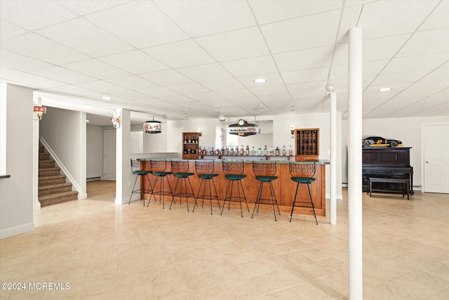 kitchen with kitchen peninsula, a paneled ceiling, hanging light fixtures, light tile patterned floors, and a kitchen breakfast bar