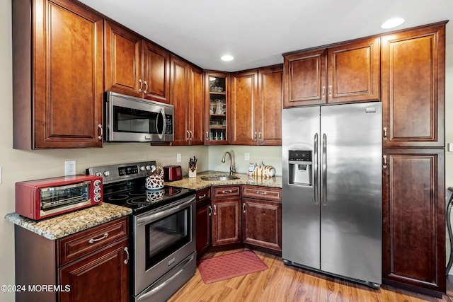 kitchen with sink, light stone counters, stainless steel appliances, and light hardwood / wood-style flooring