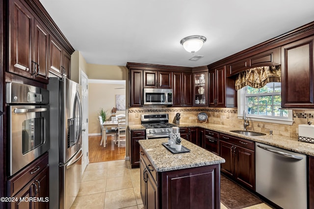 kitchen featuring light stone countertops, appliances with stainless steel finishes, a kitchen island, sink, and light tile patterned floors