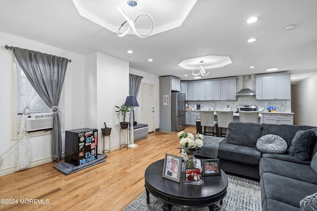 living room with an inviting chandelier, cooling unit, light wood-type flooring, and a raised ceiling