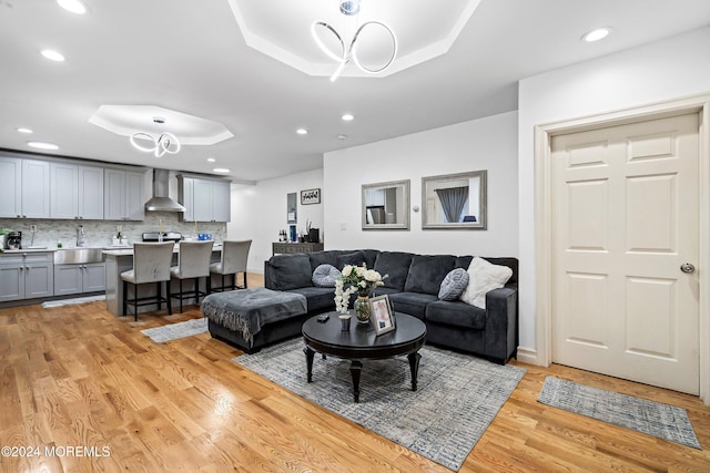 living room featuring sink, light hardwood / wood-style floors, and a raised ceiling