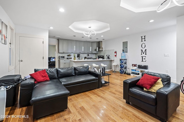 living room with electric panel, light wood-type flooring, and a raised ceiling