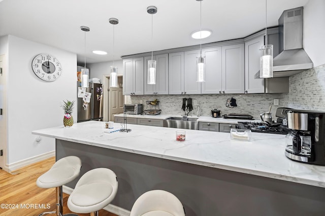 kitchen featuring gray cabinets, wall chimney exhaust hood, hanging light fixtures, and backsplash