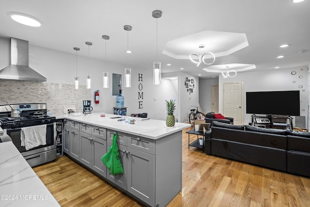 kitchen featuring stainless steel range with gas cooktop, wall chimney range hood, pendant lighting, and kitchen peninsula