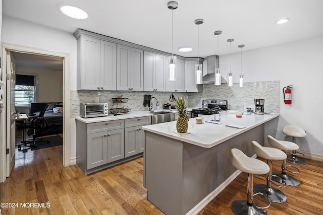 kitchen with wall chimney range hood, sink, kitchen peninsula, stainless steel range with gas cooktop, and decorative light fixtures