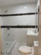 bathroom featuring a tile shower, toilet, and sink