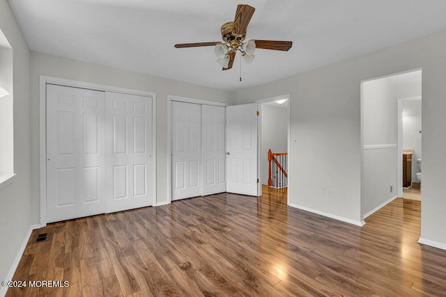 unfurnished bedroom featuring dark hardwood / wood-style flooring, multiple closets, ceiling fan, and ensuite bathroom