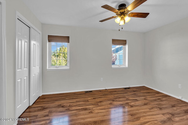 unfurnished bedroom with a closet, multiple windows, ceiling fan, and dark hardwood / wood-style floors