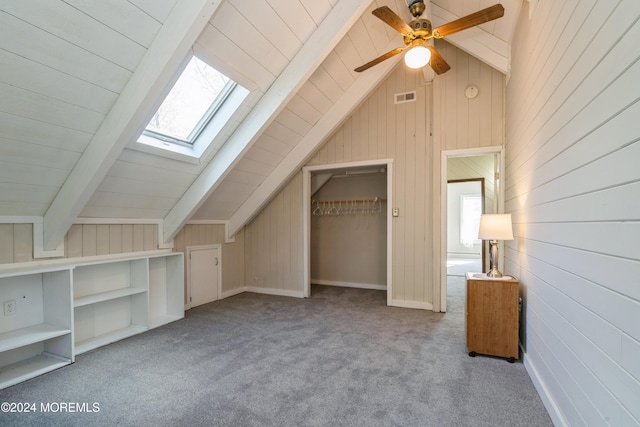 bonus room with wooden walls, vaulted ceiling with skylight, light carpet, and a wealth of natural light