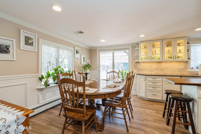 dining room with light wood-type flooring, ornamental molding, and baseboard heating