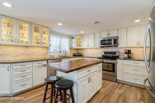 kitchen with wooden counters, white cabinets, light hardwood / wood-style flooring, appliances with stainless steel finishes, and a kitchen island