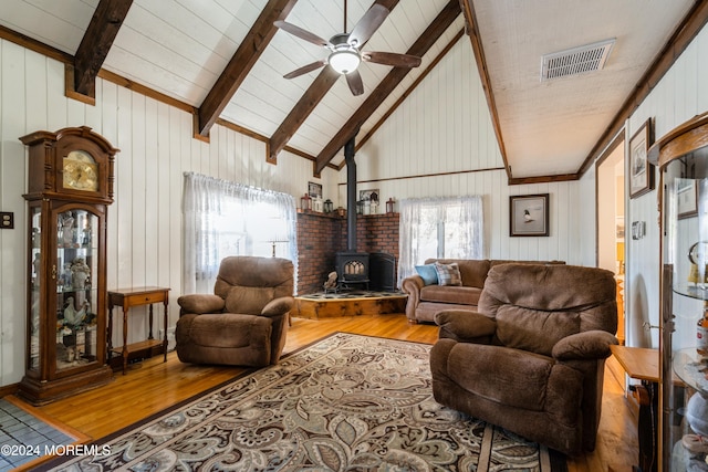 living room featuring light wood-type flooring, beam ceiling, high vaulted ceiling, a wood stove, and wood walls