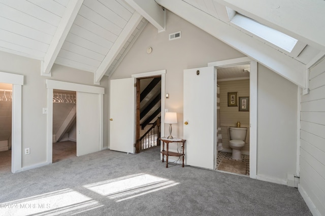 unfurnished bedroom featuring connected bathroom, wooden walls, vaulted ceiling with skylight, and carpet