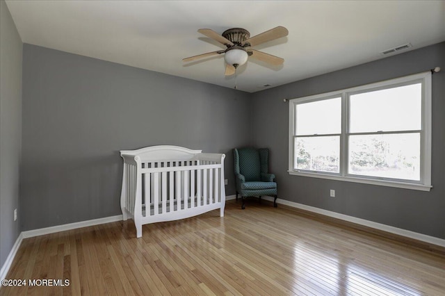 unfurnished bedroom with ceiling fan, a nursery area, and light hardwood / wood-style floors