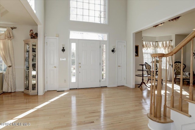 foyer featuring light wood-type flooring, a wealth of natural light, and a towering ceiling