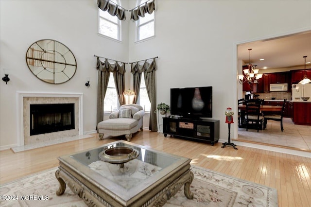 living room featuring a towering ceiling, light wood-type flooring, plenty of natural light, and a chandelier