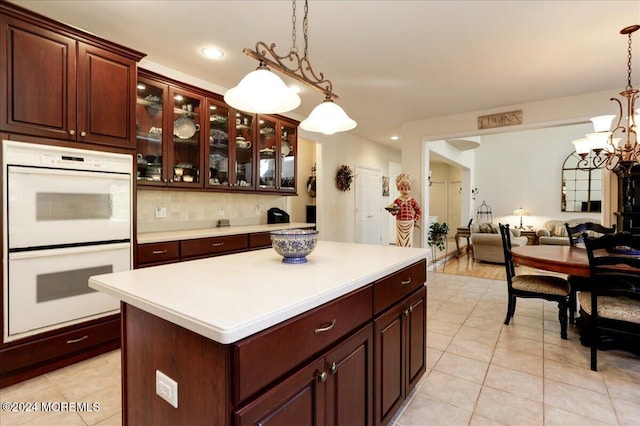 kitchen with light tile patterned flooring, backsplash, pendant lighting, an inviting chandelier, and white double oven