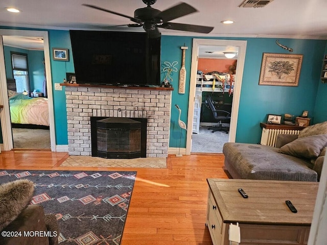 living room featuring ornamental molding, ceiling fan, a fireplace, and hardwood / wood-style flooring