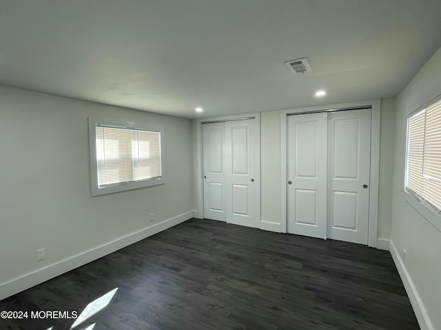 unfurnished bedroom featuring multiple windows, dark hardwood / wood-style floors, and multiple closets