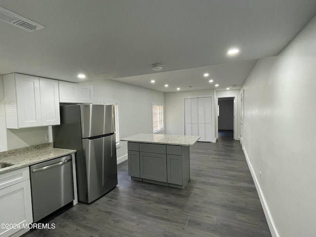 kitchen with a kitchen island, dark wood-type flooring, stainless steel appliances, white cabinets, and light stone counters