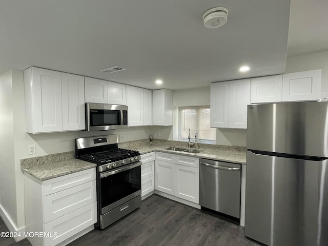 kitchen with light stone countertops, appliances with stainless steel finishes, sink, white cabinetry, and dark wood-type flooring