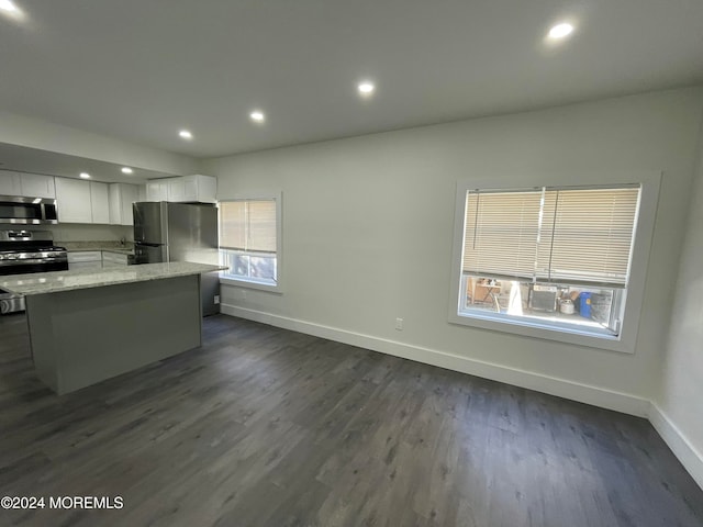 kitchen with dark wood-type flooring, stainless steel appliances, light stone countertops, a center island, and white cabinets