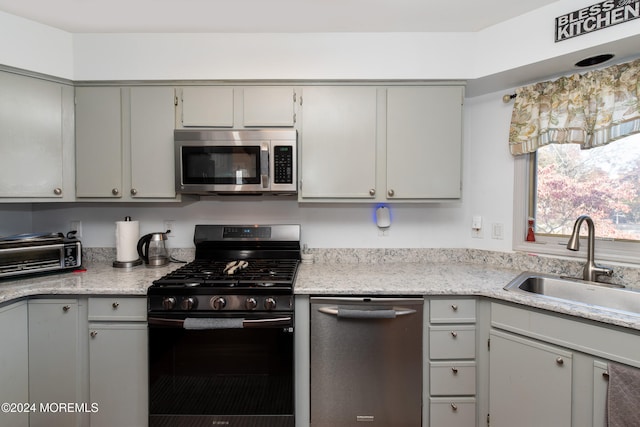 kitchen featuring gray cabinets, light stone countertops, stainless steel appliances, and sink