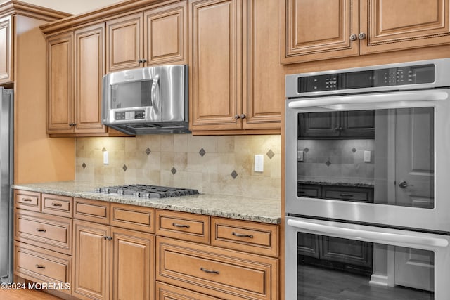 kitchen featuring light stone countertops, decorative backsplash, appliances with stainless steel finishes, and wood-type flooring