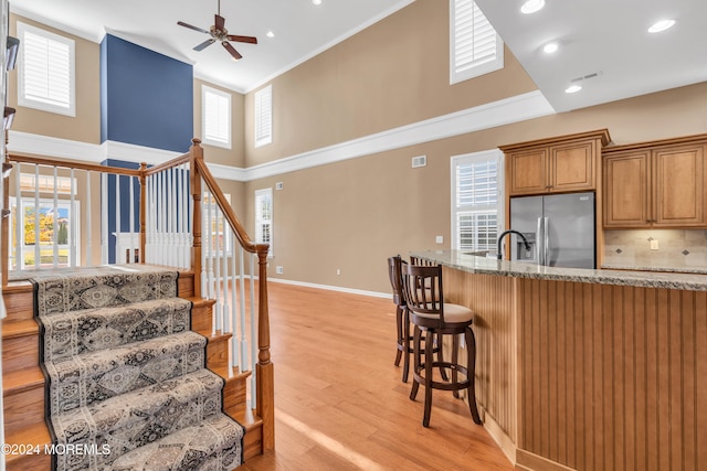 kitchen with a towering ceiling, light wood-type flooring, plenty of natural light, and stainless steel fridge with ice dispenser