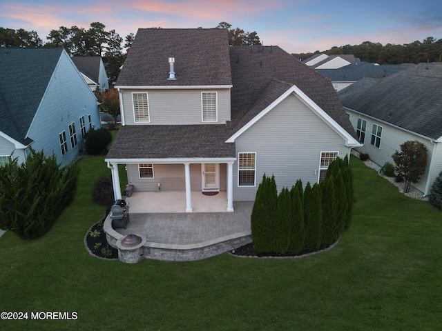 back house at dusk with a patio area and a lawn