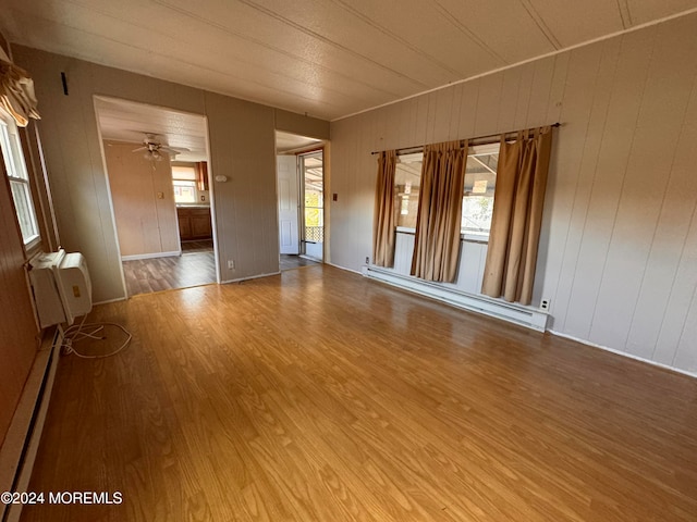 empty room featuring wood walls, ceiling fan, a baseboard radiator, and hardwood / wood-style flooring