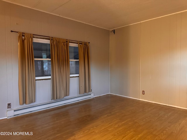 spare room featuring a baseboard radiator, hardwood / wood-style flooring, and wooden walls