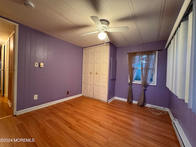 unfurnished bedroom featuring ceiling fan, baseboard heating, wood-type flooring, a textured ceiling, and wooden walls