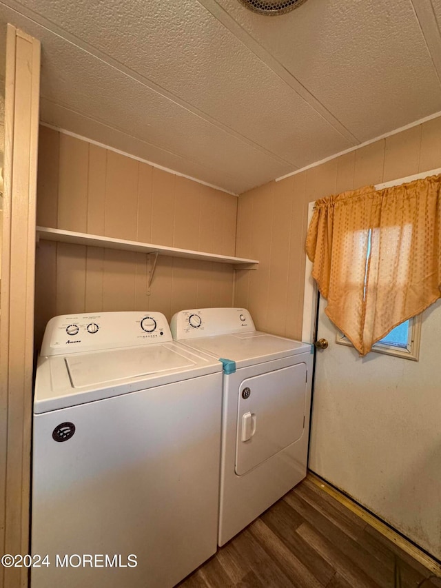 clothes washing area featuring wood-type flooring, washing machine and dryer, a textured ceiling, and wooden walls