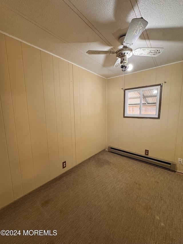 carpeted empty room with ceiling fan, wood walls, a textured ceiling, and a baseboard heating unit