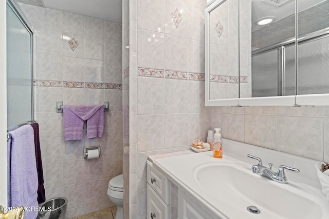 bathroom with tile walls, vanity, toilet, and a shower with door