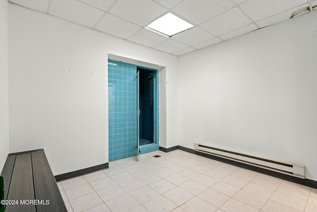 unfurnished room featuring a paneled ceiling, baseboard heating, and light tile patterned floors