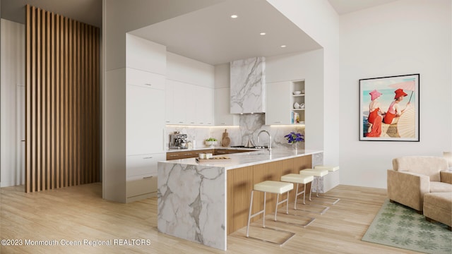 kitchen featuring a breakfast bar area, kitchen peninsula, backsplash, white cabinetry, and light hardwood / wood-style floors