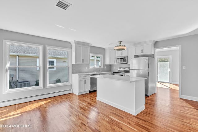 kitchen with appliances with stainless steel finishes, a kitchen island, light wood-type flooring, and a wealth of natural light