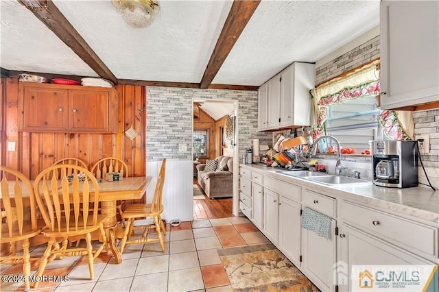 kitchen featuring beam ceiling, white cabinetry, a textured ceiling, sink, and brick wall