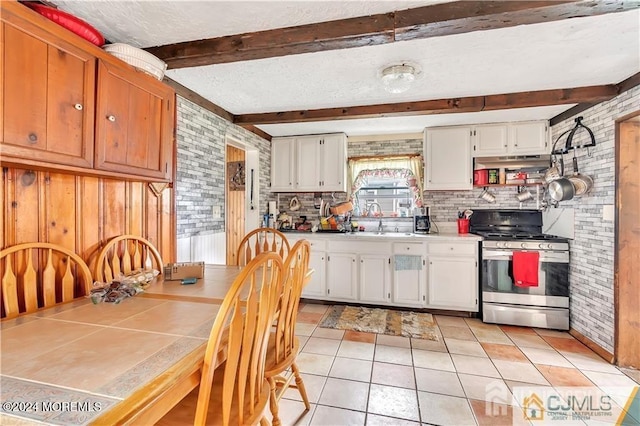 kitchen with wood walls, sink, stainless steel range oven, white cabinets, and beam ceiling