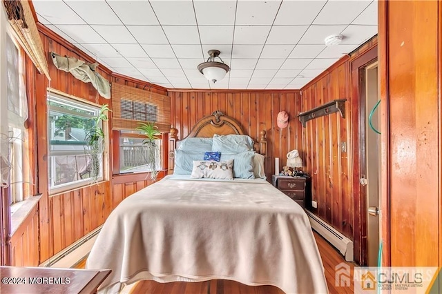 bedroom with wooden walls, wood-type flooring, and a baseboard radiator