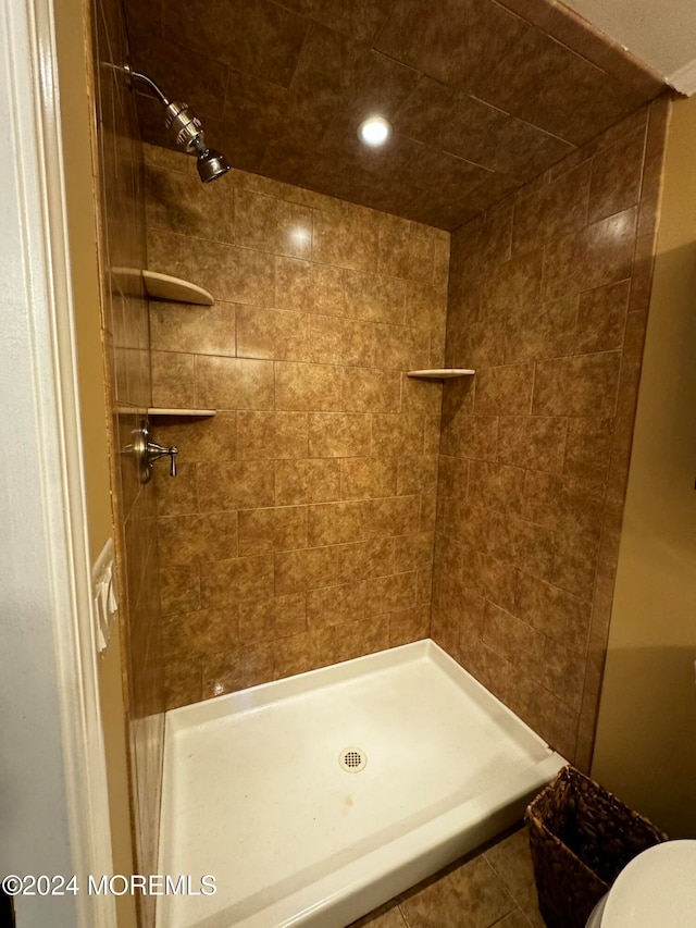 bathroom with a tile shower, toilet, and tile patterned floors