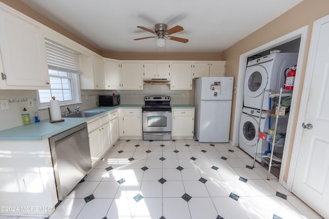 kitchen with stainless steel appliances, white cabinetry, sink, and stacked washer / dryer