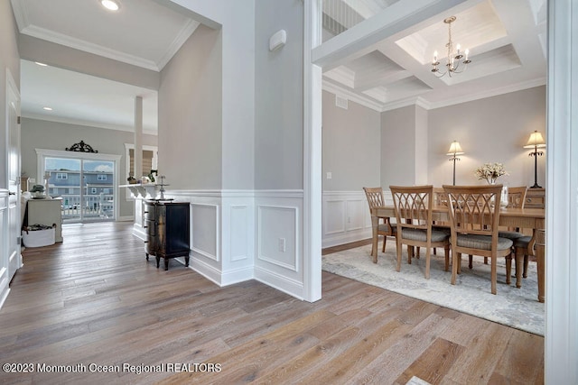 dining area featuring a notable chandelier, ornamental molding, coffered ceiling, and light wood-type flooring