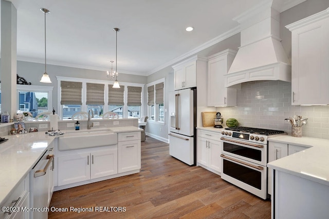 kitchen with premium range hood, pendant lighting, high quality appliances, white cabinetry, and sink